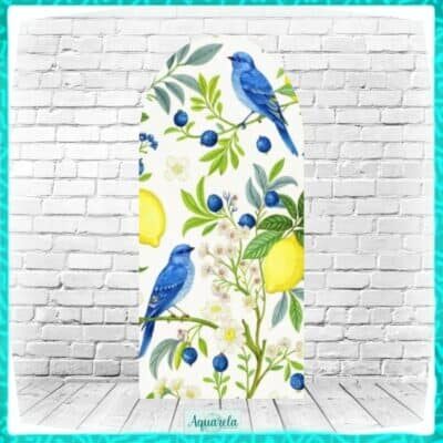 Prancha de surfe de madeira com estampa floral azul e amarela, incluindo pássaros azuis, contra parede de tijolos brancos.
